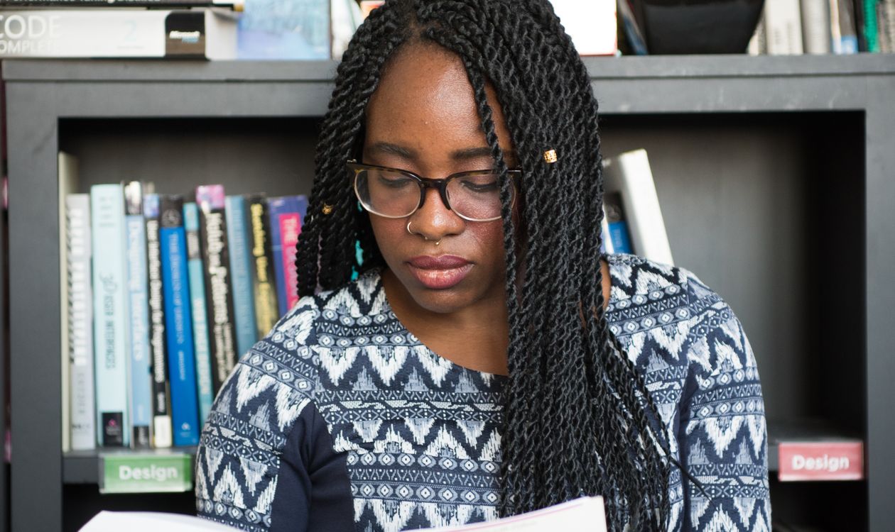 African author reading an e-book on a laptop surrounded by books in a library